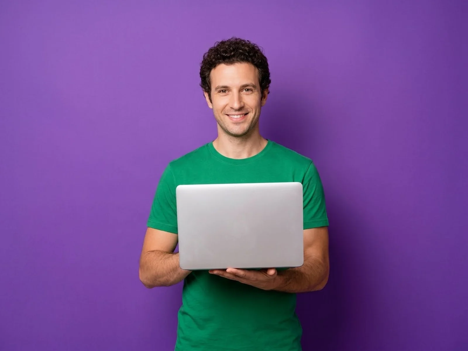 A smiling man holding an open laptop against a solid violet background