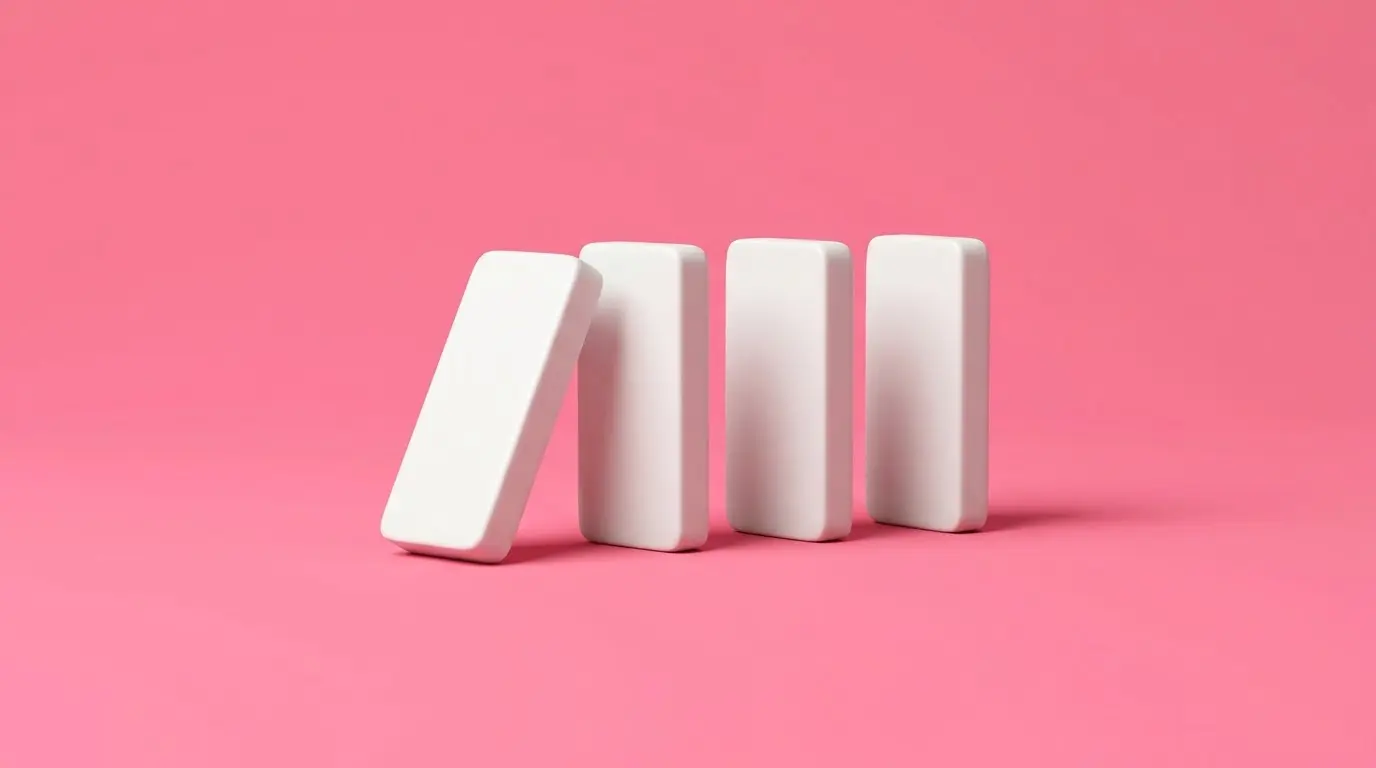 A row of four dominoes with the first one tipping, on a pink background